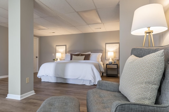 bedroom featuring a paneled ceiling, dark wood-style flooring, and baseboards