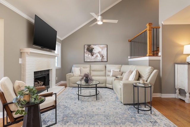 living area featuring baseboards, ceiling fan, crown molding, light wood-type flooring, and a brick fireplace