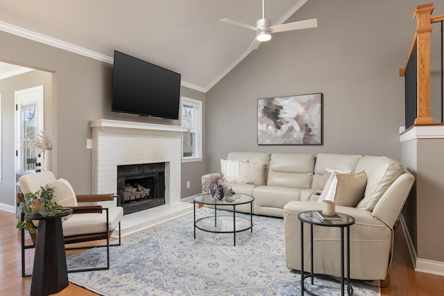 living room with a fireplace, ornamental molding, vaulted ceiling, ceiling fan, and wood finished floors