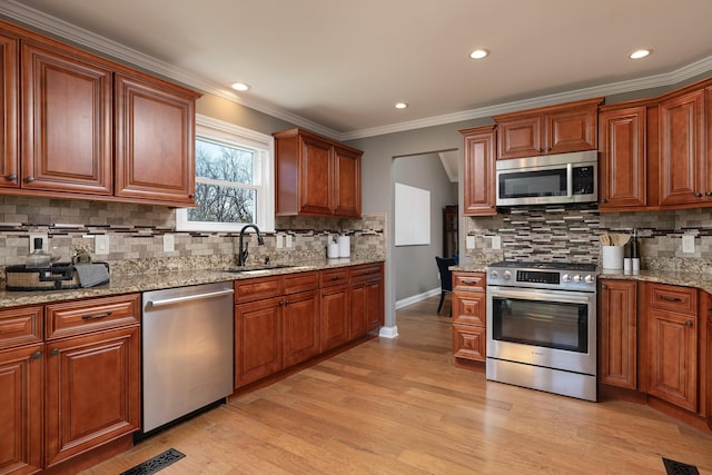 kitchen with light stone counters, stainless steel appliances, a sink, light wood-style floors, and ornamental molding