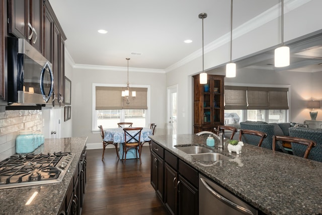 kitchen with appliances with stainless steel finishes, sink, dark stone counters, hanging light fixtures, and crown molding