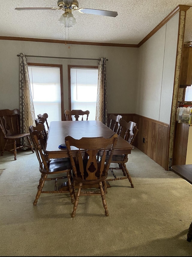 carpeted dining room with a textured ceiling, wooden walls, crown molding, and a wainscoted wall