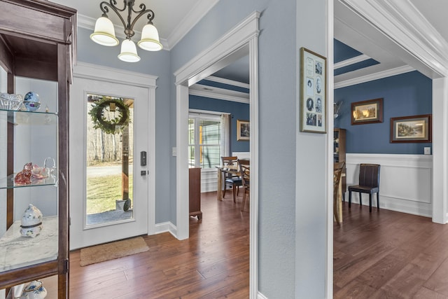 foyer entrance with a notable chandelier, dark wood-style flooring, a wainscoted wall, and crown molding