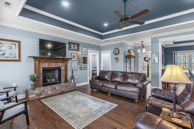 living area with a tray ceiling, a brick fireplace, visible vents, and wood finished floors