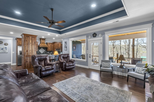 living area with baseboards, a tray ceiling, dark wood-style flooring, and crown molding