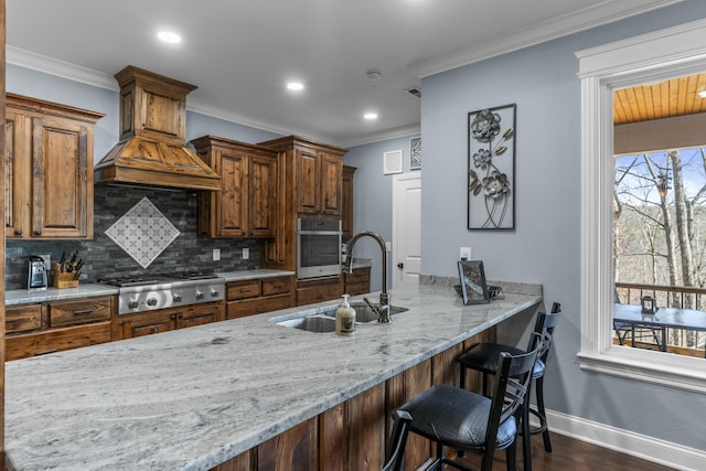 kitchen with custom range hood, appliances with stainless steel finishes, a sink, light stone countertops, and backsplash