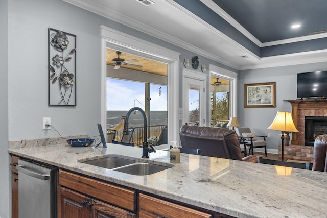 kitchen with ornamental molding, open floor plan, stainless steel dishwasher, a brick fireplace, and a sink