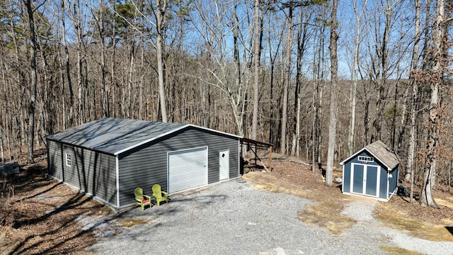 detached garage with driveway, a forest view, and a storage shed