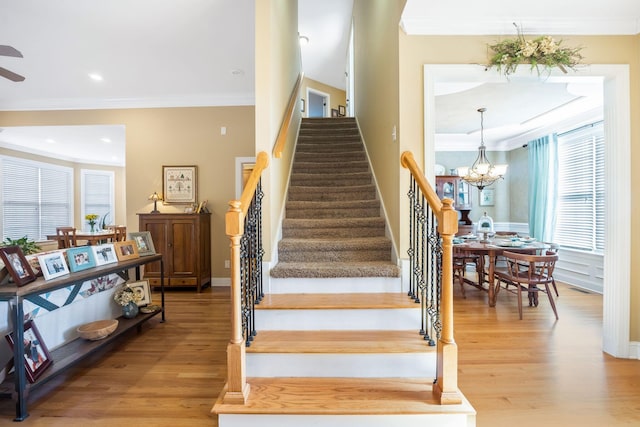 stairs with baseboards, ornamental molding, wood finished floors, and a notable chandelier