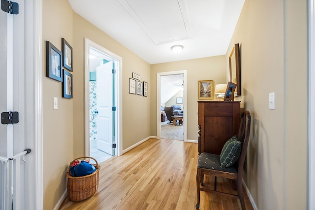 corridor with light wood finished floors, attic access, and baseboards