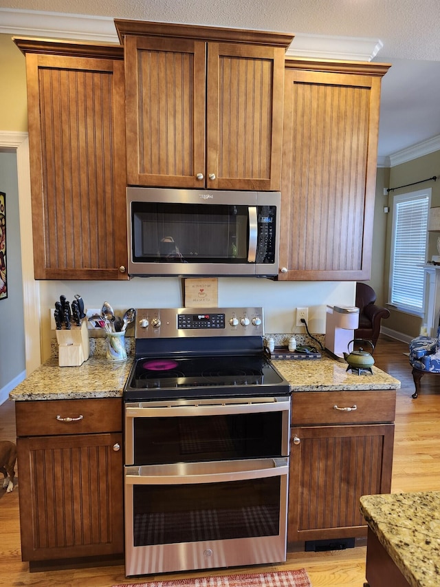 kitchen with brown cabinetry, light stone countertops, stainless steel appliances, crown molding, and light wood-type flooring