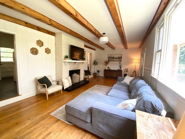 living room featuring wood-type flooring, a brick fireplace, and beam ceiling