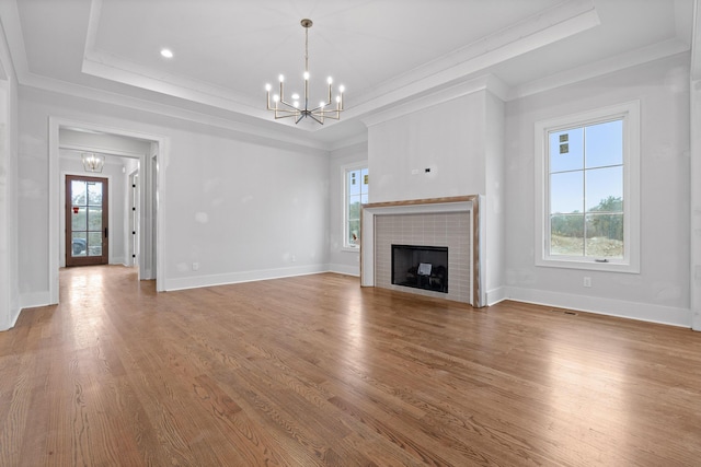 unfurnished living room with an inviting chandelier, a tray ceiling, crown molding, and hardwood / wood-style flooring