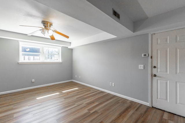 empty room with a ceiling fan, wood finished floors, visible vents, and baseboards