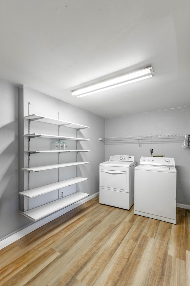 laundry area with laundry area, baseboards, washing machine and clothes dryer, and wood finished floors