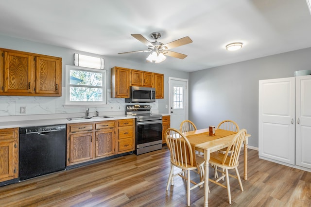 kitchen featuring appliances with stainless steel finishes, light wood-type flooring, brown cabinetry, and a sink