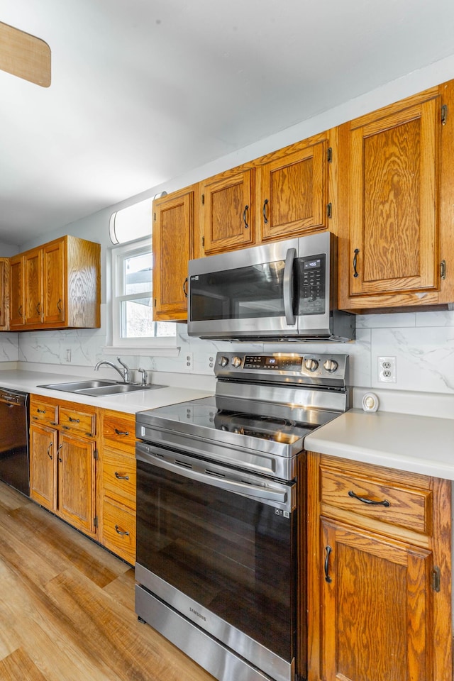 kitchen featuring stainless steel appliances, a sink, light countertops, backsplash, and brown cabinetry