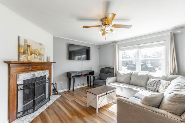 living room with ornamental molding, a high end fireplace, ceiling fan, wood finished floors, and baseboards