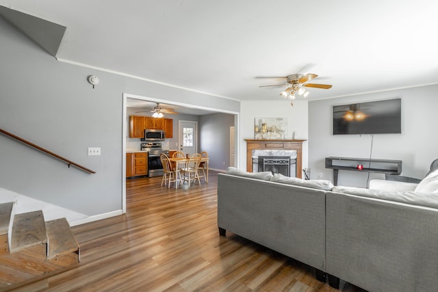 living room with ceiling fan, a fireplace, baseboards, and wood finished floors