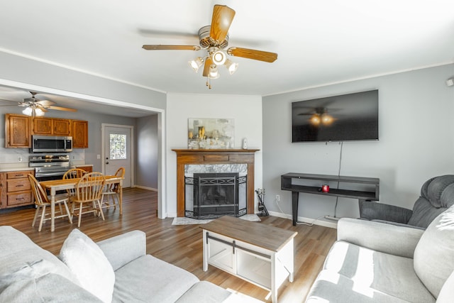 living room with ornamental molding, a high end fireplace, ceiling fan, wood finished floors, and baseboards