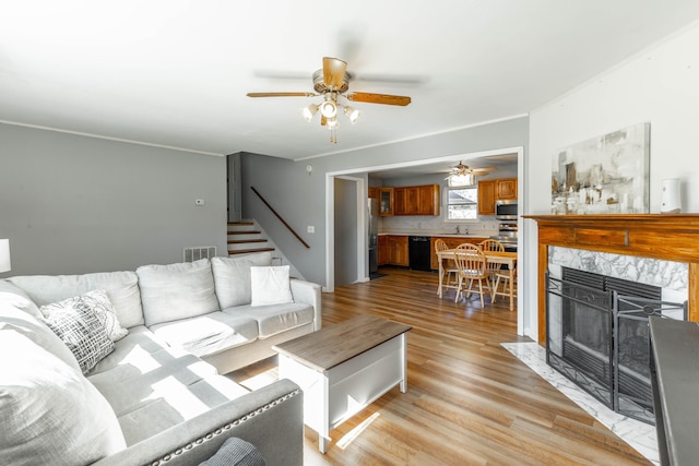 living area featuring visible vents, ceiling fan, stairway, light wood-style floors, and a fireplace