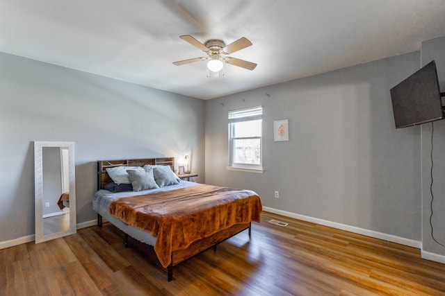 bedroom featuring a ceiling fan, wood finished floors, visible vents, and baseboards