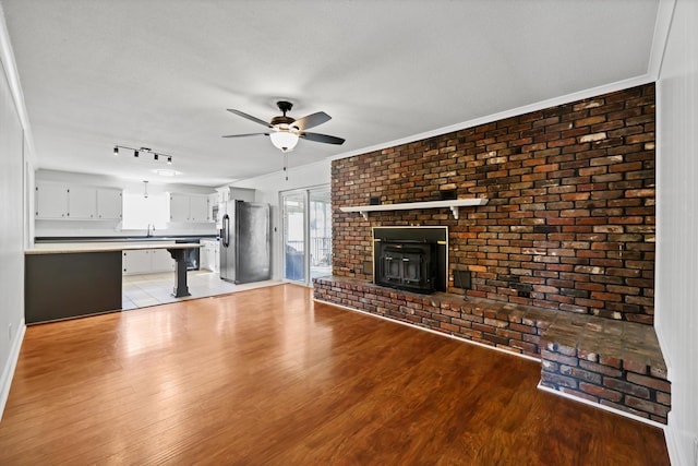 unfurnished living room featuring a textured ceiling, brick wall, a ceiling fan, light wood-style floors, and a wood stove