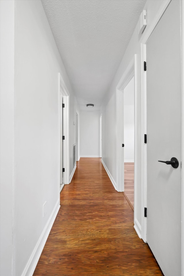 hallway with dark wood-style flooring, visible vents, a textured ceiling, and baseboards