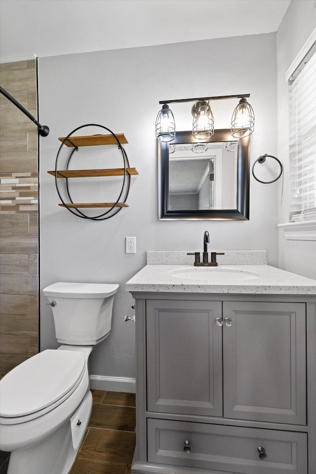 bathroom featuring baseboards, toilet, wood tiled floor, a tile shower, and vanity