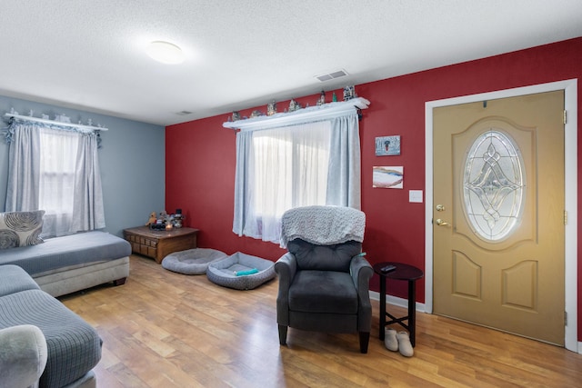 interior space featuring baseboards, a textured ceiling, visible vents, and wood finished floors