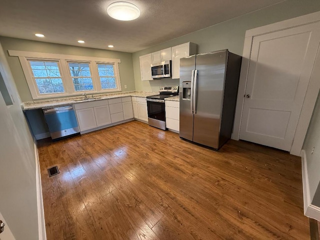 kitchen featuring sink, white cabinetry, appliances with stainless steel finishes, light stone countertops, and light hardwood / wood-style floors