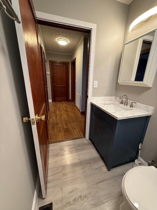 bathroom featuring vanity, wood-type flooring, toilet, and a textured ceiling