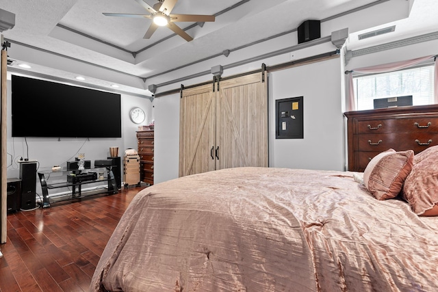 bedroom featuring dark wood-type flooring, a raised ceiling, ceiling fan, and a barn door