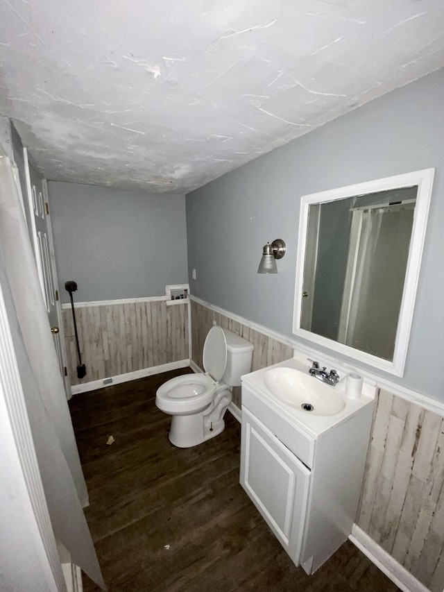 bathroom with hardwood / wood-style flooring, vanity, wood walls, and toilet