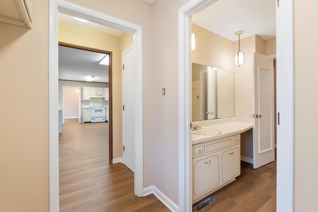 corridor featuring a sink, baseboards, and light wood-style floors