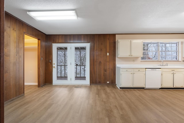 kitchen featuring white dishwasher, wood walls, a sink, light countertops, and light wood-type flooring