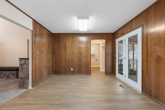 spare room featuring baseboards, visible vents, wooden walls, and light wood-style flooring