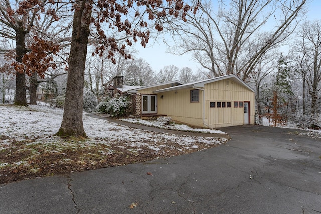 view of snowy exterior with an attached garage, a chimney, and aphalt driveway