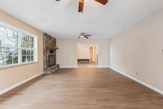 unfurnished living room featuring a stone fireplace, light wood-type flooring, a ceiling fan, and baseboards