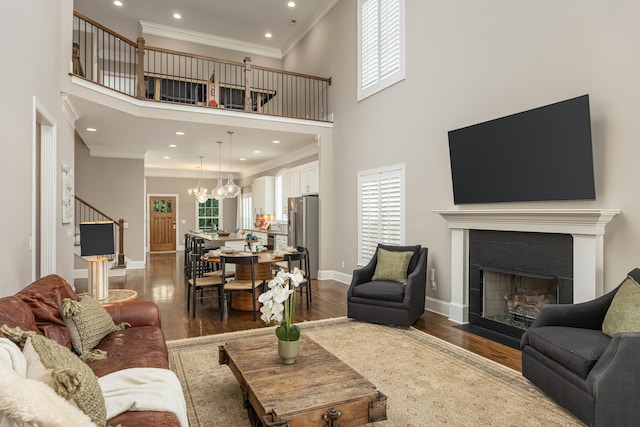 living room featuring wood-type flooring, a chandelier, ornamental molding, a tile fireplace, and a towering ceiling