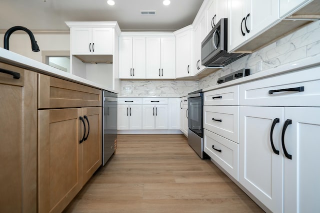 kitchen with tasteful backsplash, light wood-type flooring, white cabinets, and appliances with stainless steel finishes