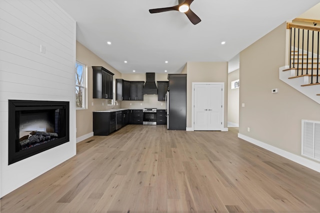 unfurnished living room with a sink, visible vents, baseboards, stairway, and light wood-type flooring