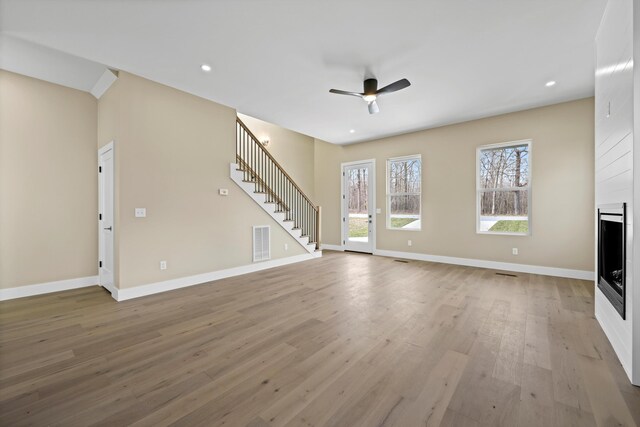 unfurnished living room with visible vents, stairway, ceiling fan, light wood-type flooring, and baseboards