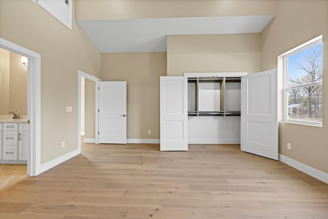 unfurnished bedroom featuring light wood-type flooring, a sink, baseboards, and a closet