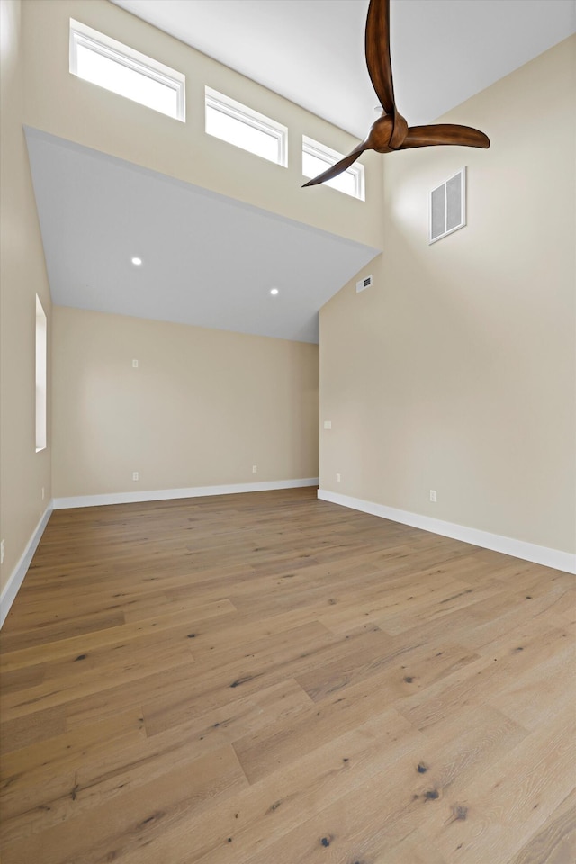 spare room with light wood-style flooring, a high ceiling, visible vents, and baseboards