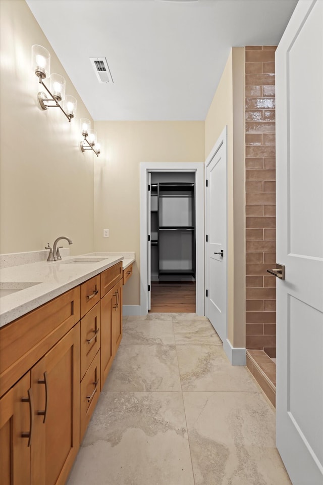 full bathroom featuring double vanity, baseboards, visible vents, tiled shower, and a sink