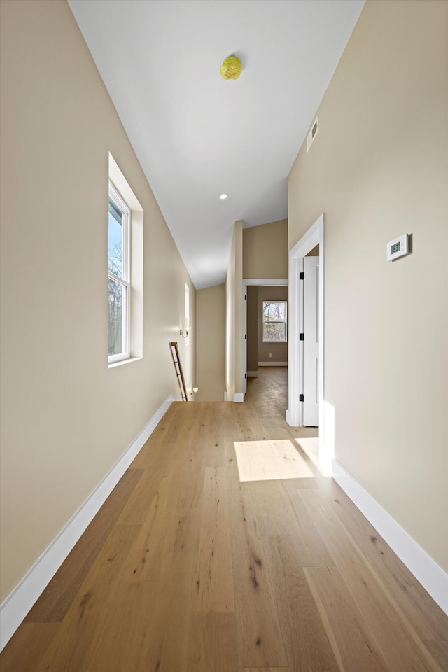 hallway with light wood-style floors, visible vents, a wealth of natural light, and an upstairs landing