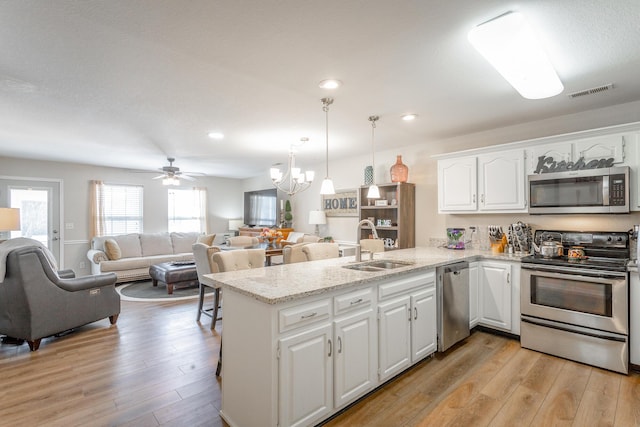 kitchen featuring appliances with stainless steel finishes, white cabinets, decorative light fixtures, sink, and kitchen peninsula