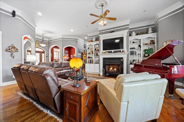 living room featuring a lit fireplace, arched walkways, dark wood finished floors, and ornamental molding