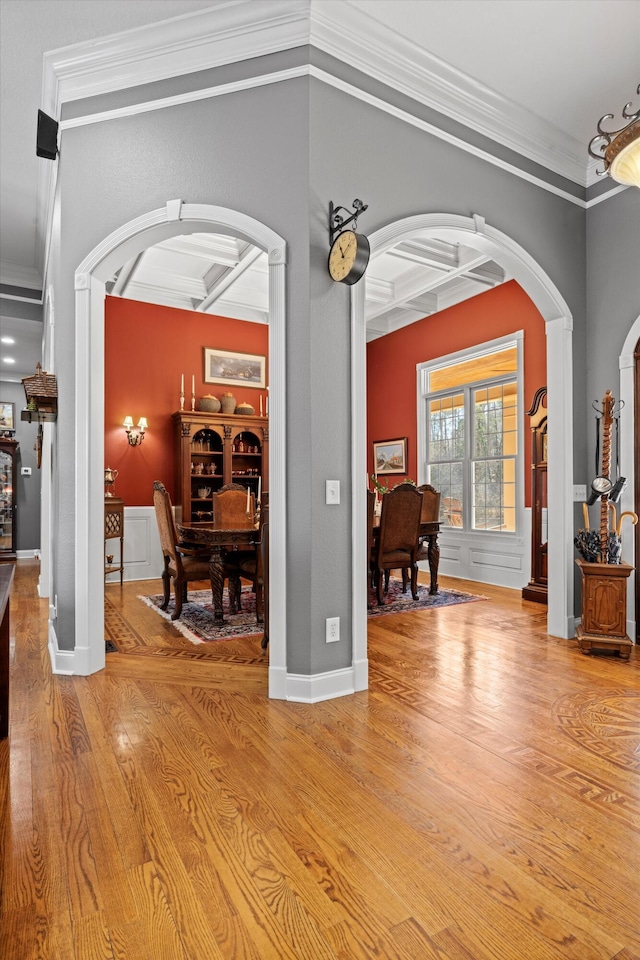 interior space featuring baseboards, arched walkways, coffered ceiling, beamed ceiling, and light wood-style floors